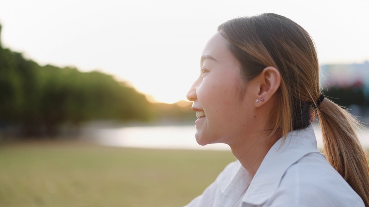 年轻快乐的亚洲女性坐在公园里，一边用手机网购。科技与电子商务概念视频素材