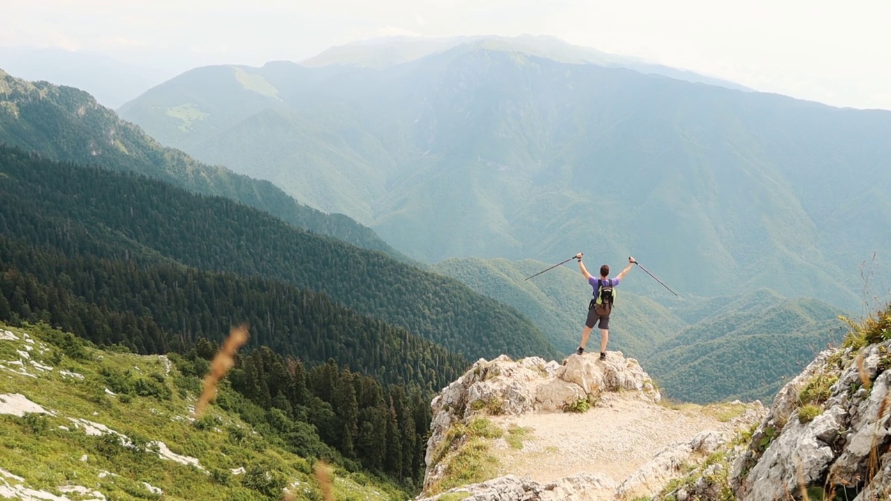 在山上庆祝成功——一名男子爬到山顶，用登山杖高举双手视频素材