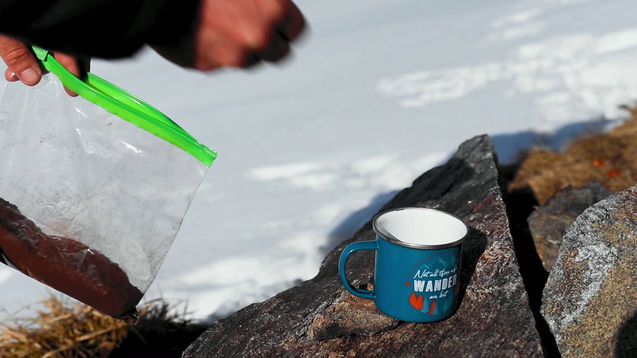 在户外雪山上，有人往杯子里倒咖啡粉的高清画面视频素材