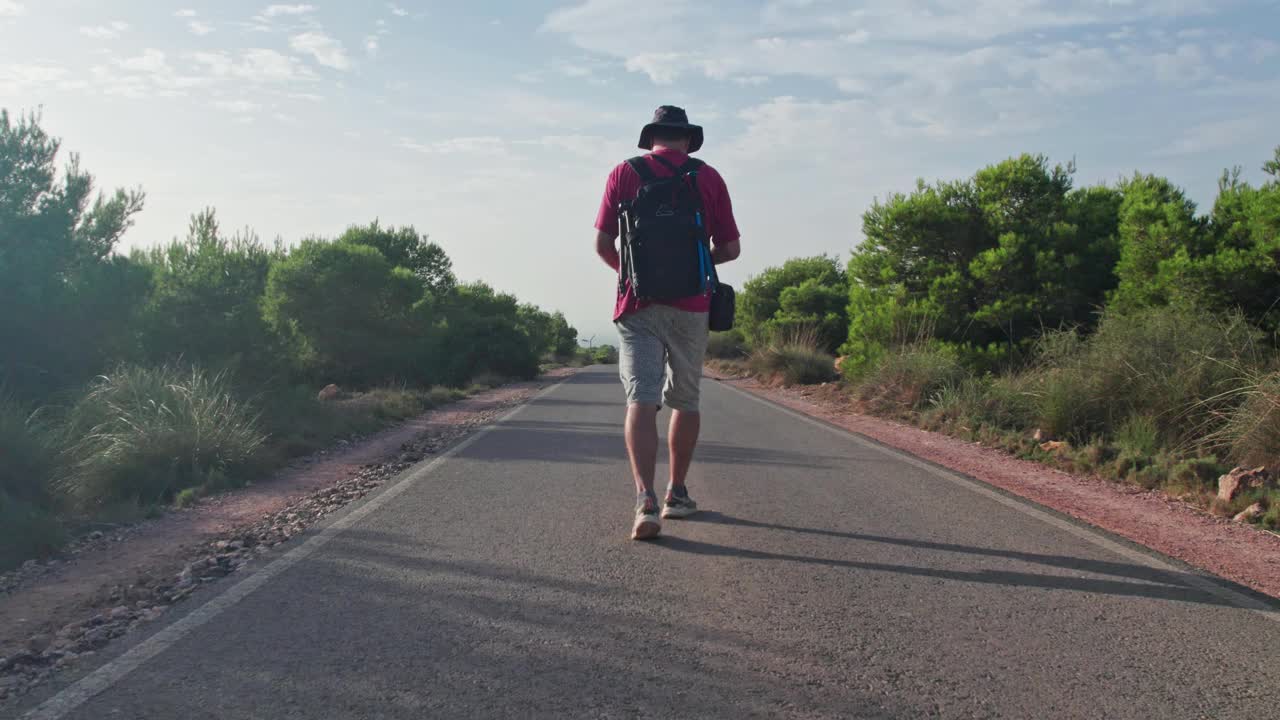 镜头跟随一个旅行或冒险的男人，一个年轻的千禧一代旅行者沿着柏油路到达他的目的地。视频素材