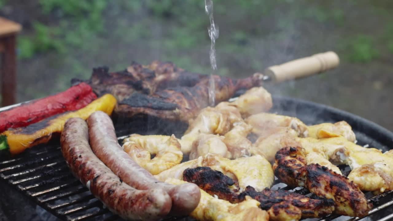 把水倒在烤架上烤的鸡翅、香肠和牛排上。视频素材