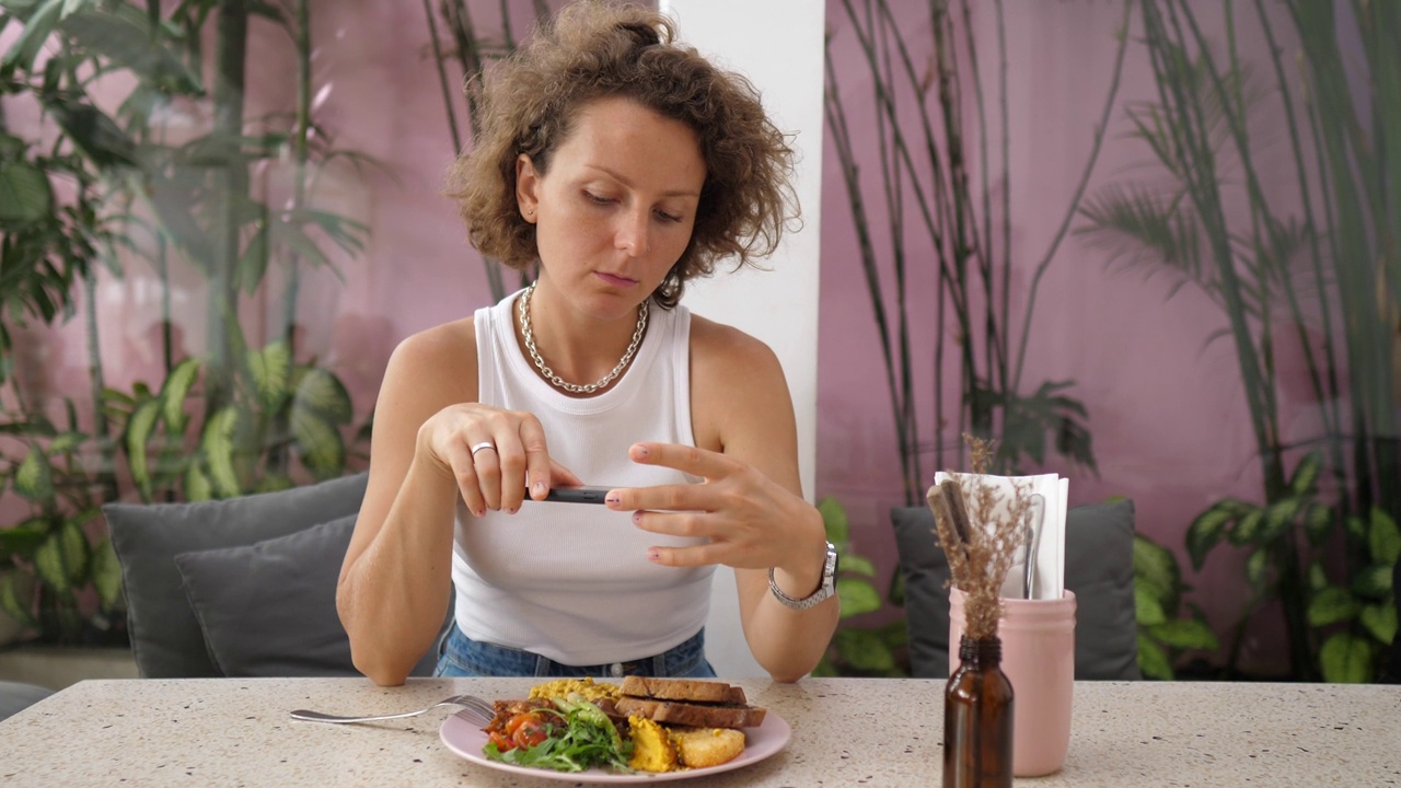 一位女博主在一家时髦的咖啡馆独自吃早餐时，拍下了她的健康食品照片，想要在社交媒体上分享她的内容。视频素材