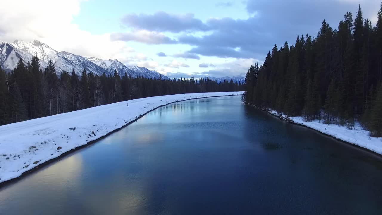 美丽的冬季景观，雪山和河流在多云的天空下视频素材