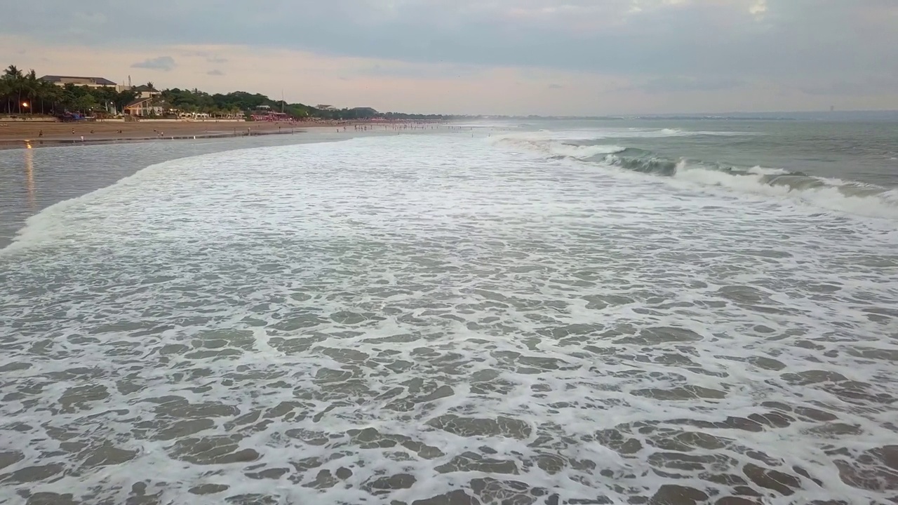 4K无人机拍摄的海浪在巴厘岛的海滩海岸线。海浪拍打的印度洋和背景是漂亮房子的海滩视频素材