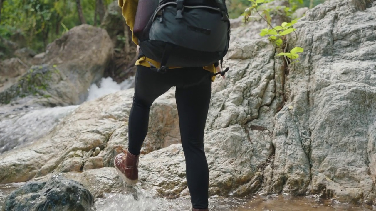 亚洲年轻女子徒步旅行和背包穿着黄色毛衣和靴子走在瀑布森林的石头视频素材