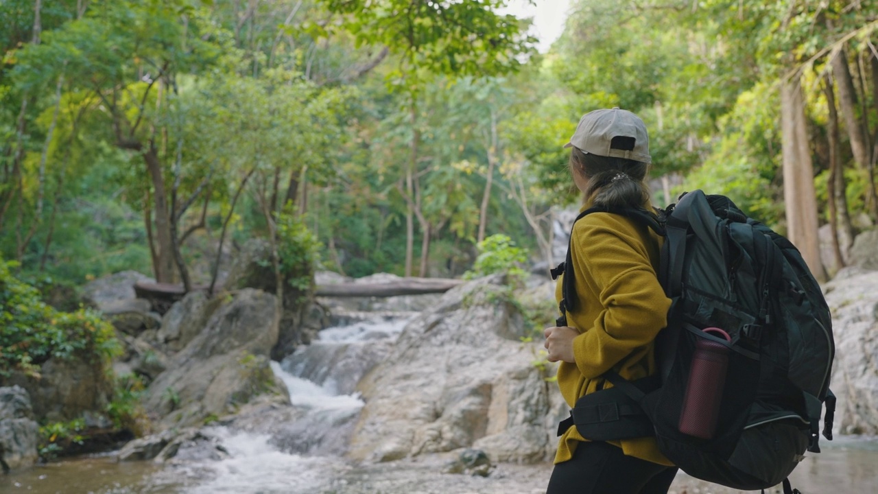 亚洲年轻女子徒步旅行和背包穿着黄色毛衣行走和站在森林呼吸新鲜空气视频素材