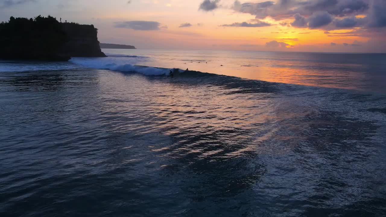 航拍的海洋与波浪，冲浪者和色彩斑斓的日落或日出在巴厘岛。视频素材