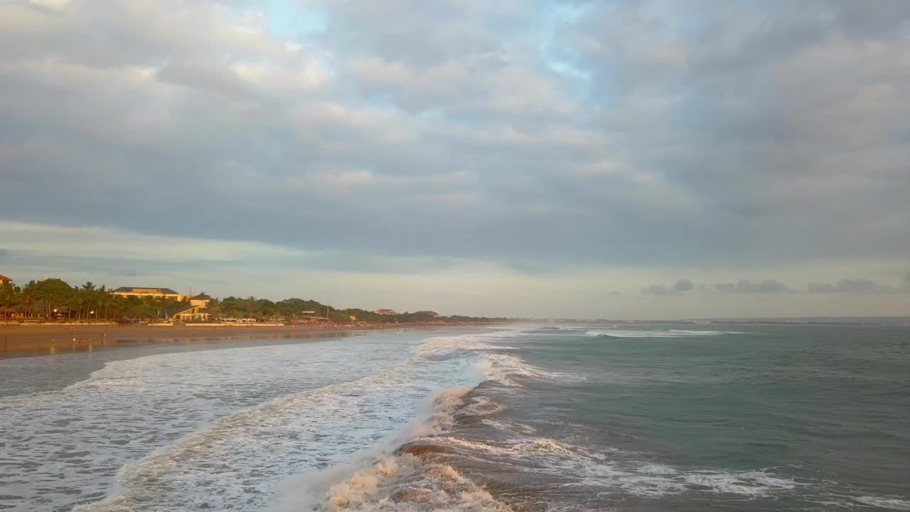 4K无人机拍摄的海浪在巴厘岛的海滩海岸线。海浪拍打的印度洋和背景是漂亮房子的海滩视频素材