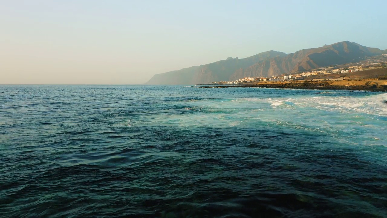 暴风雨天气下，无人机在海面低空飞行。海浪泡沫飞溅。岩石海岸。背景是洛斯吉甘特悬崖。特内里费。蓝绿色大西洋水域的美丽景色。金丝雀。视频素材