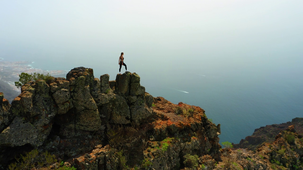 勇敢坚强的女子徒步旅行者站在山顶的悬崖边缘。El agujero, Los Gigantes, Tenerife。山顶上的少女，青春幸福。美丽的海洋景观。去哪儿都可以。天线。视频素材