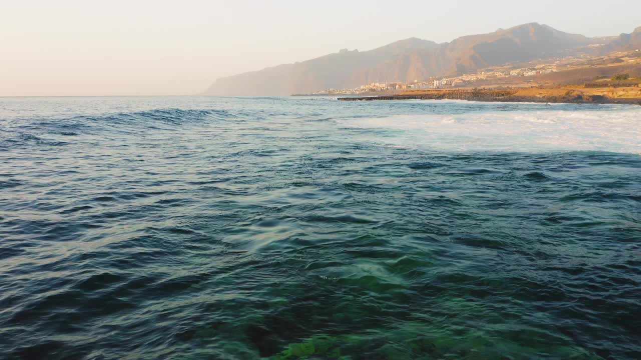 深蓝色的大海，水面起波纹，大风引起的巨浪涌向洛斯·吉甘特海岸。小度假胜地，日落时有巨大的悬崖视频素材