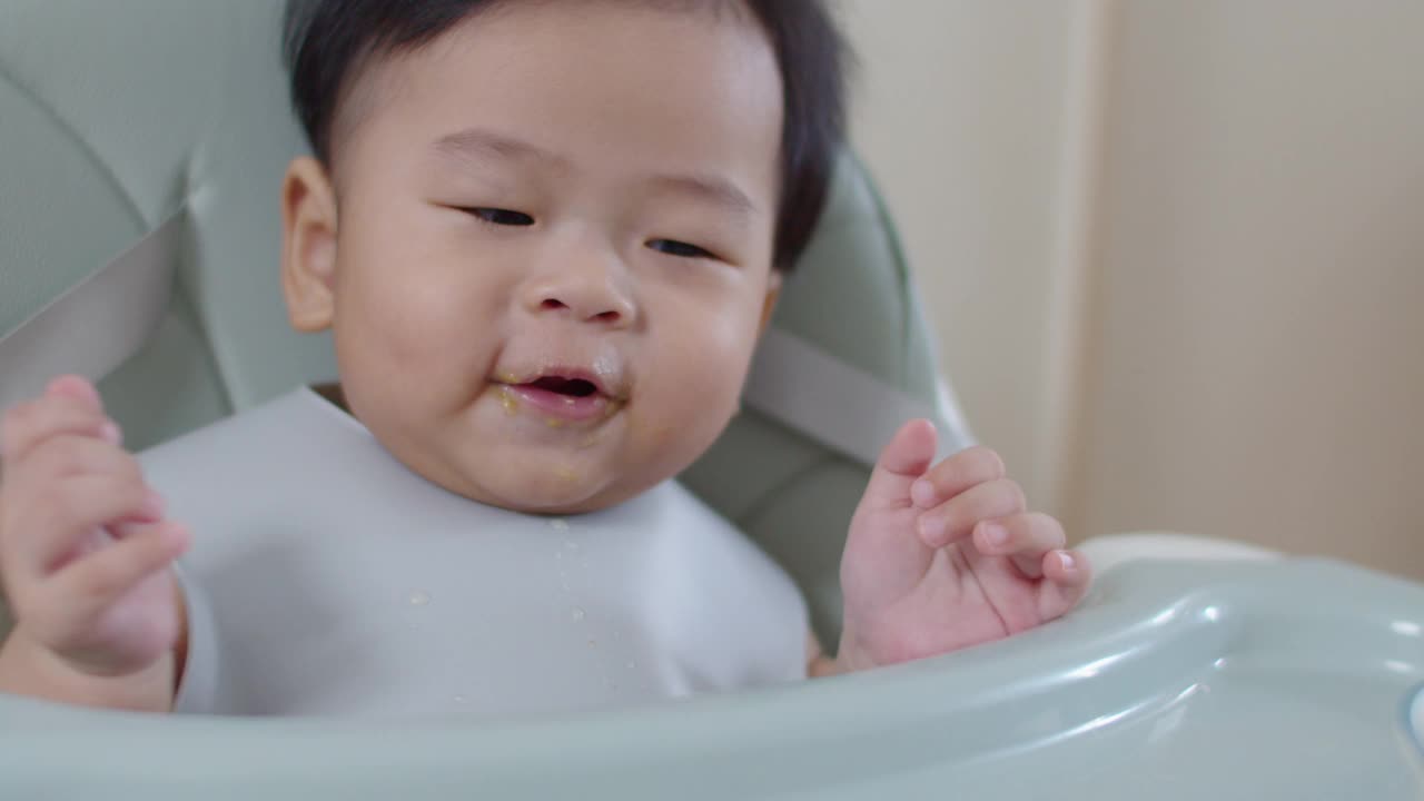 坐在高脚椅上的亚洲小男孩被妈妈喂食物。视频素材