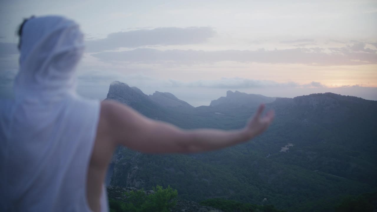 兜帽男站在世界之巅。从悬崖上欣赏美景，庆祝成功视频素材