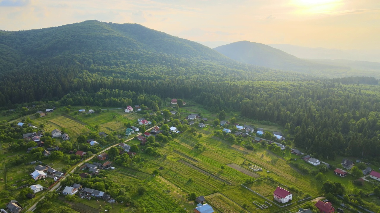 傍晚雾蒙蒙的鸟瞰图，在明亮的夕阳下，在高高的山峰之间的小山村的房子和深色的松林。黄昏时分野山林地的迷人景色视频素材