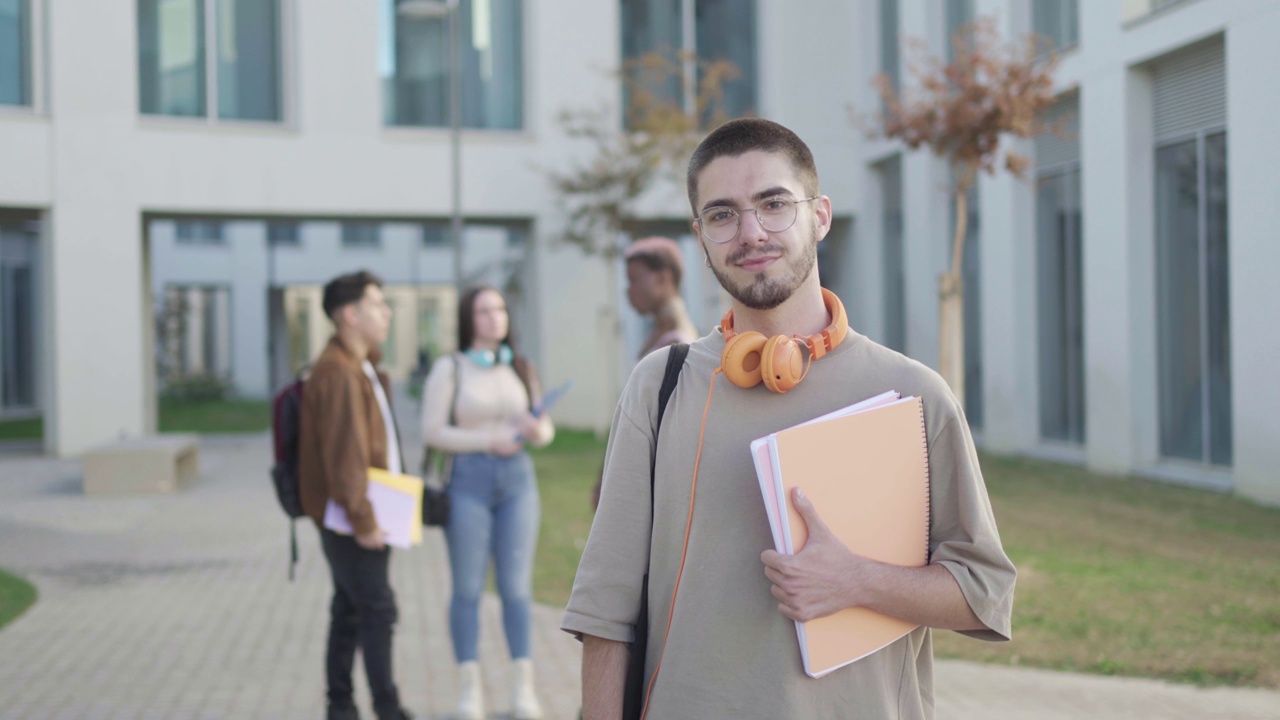 大学校园里，一个男生看着镜头，而他的朋友们在后面聊天视频素材