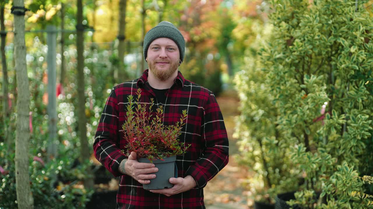 一个快乐的花园中心工作人员拿着一盆植物的肖像视频素材