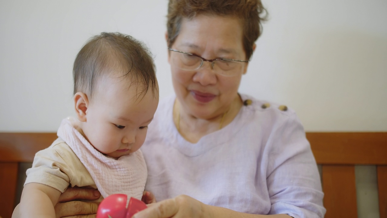 快乐放松的高级亚洲老年妇女拥抱，抱着婴儿，蹒跚学步的孩子，孙女，拥抱，坐在家里的沙发上。几代人的家庭，祖父母和孙子一起享受时光视频素材