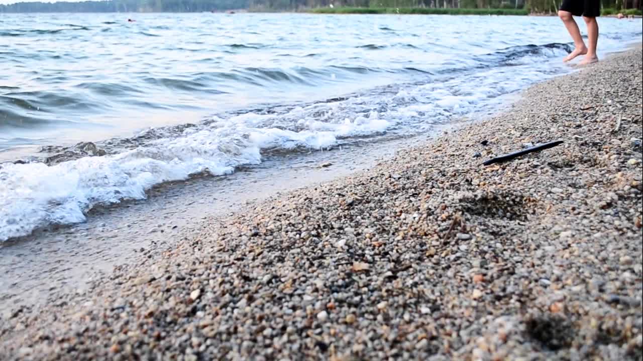 一个孩子赤脚走在海滩上的海浪，脚部按摩放松。视频下载