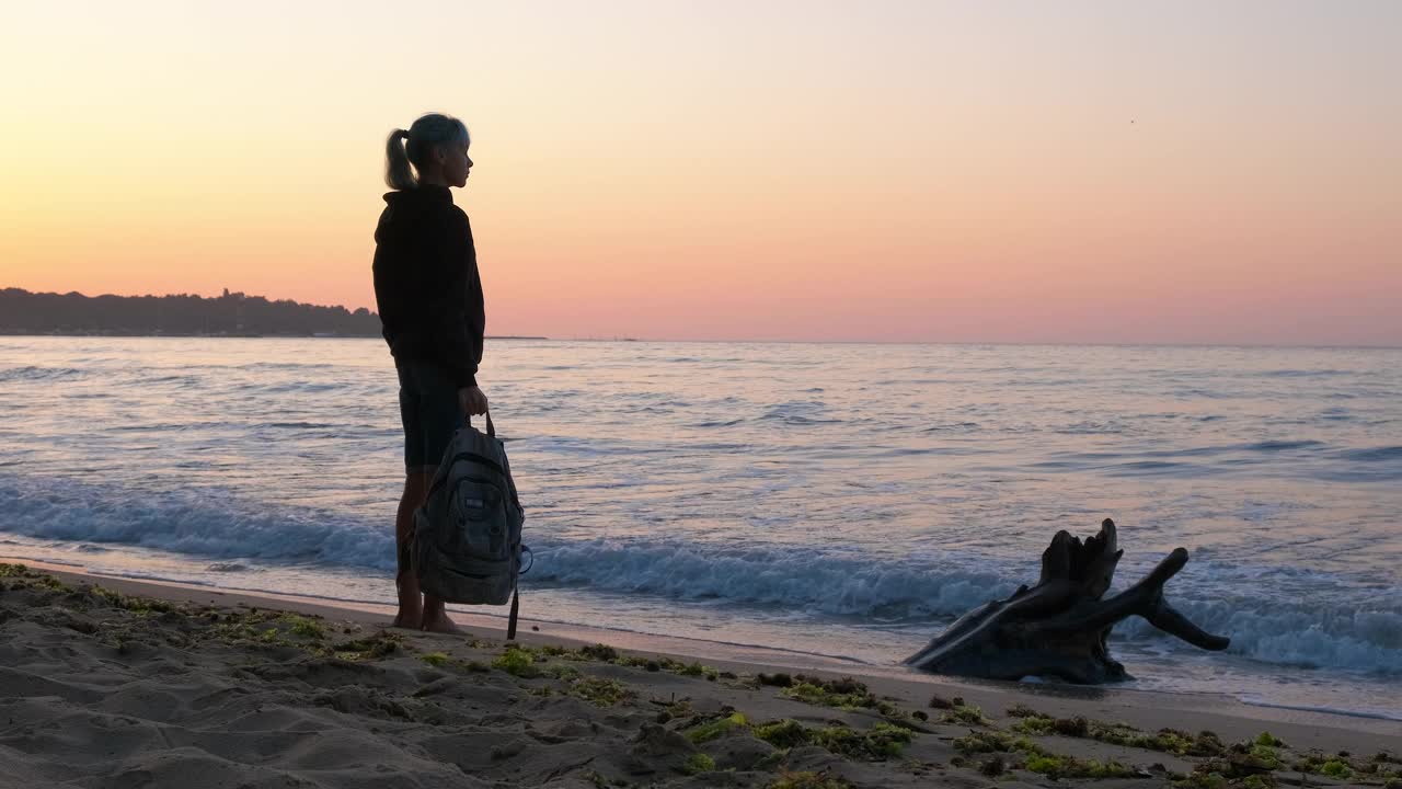 女孩看着夕阳在空旷的海岸。视频素材