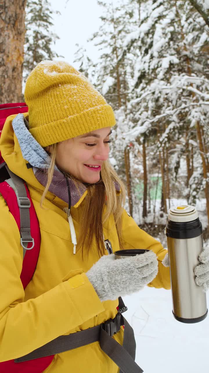 一名年轻女子在冬季森林徒步旅行时，用保温杯倒茶喝。视频素材