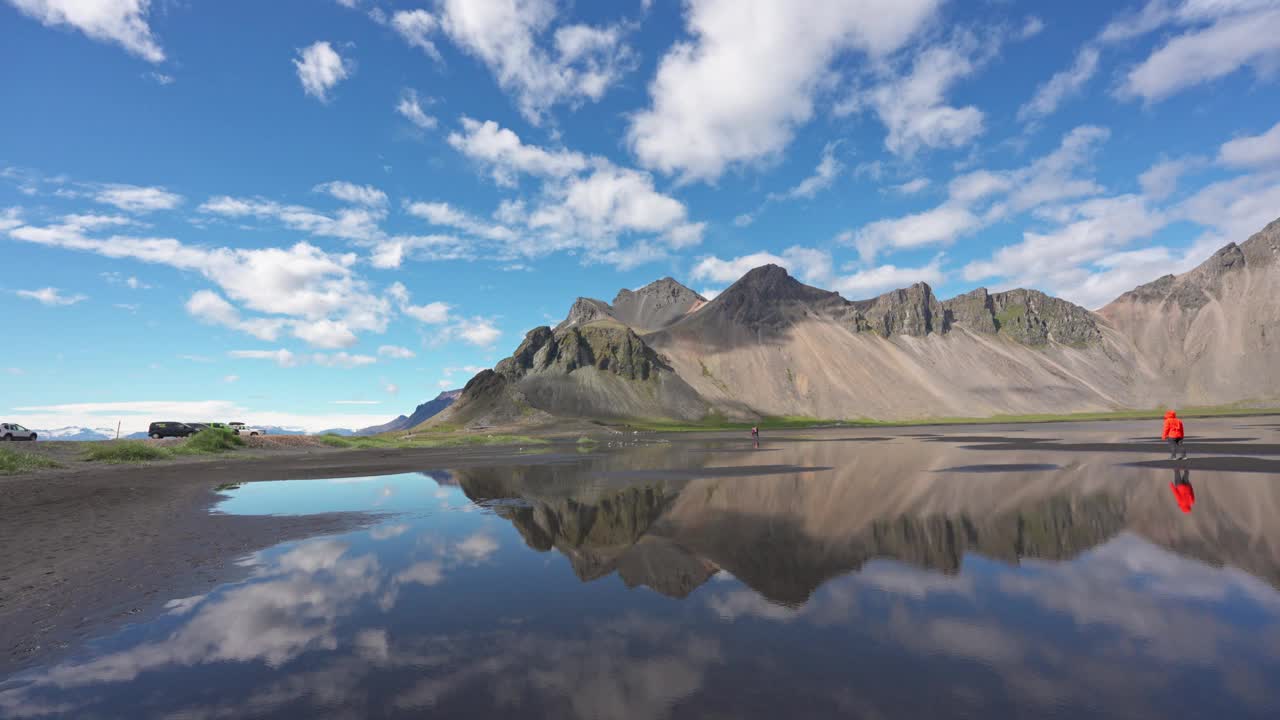 在冰岛Stokksnes半岛阳光明媚的黑色沙滩上，Vestrahorn山的景观与游客的旅行反射视频素材