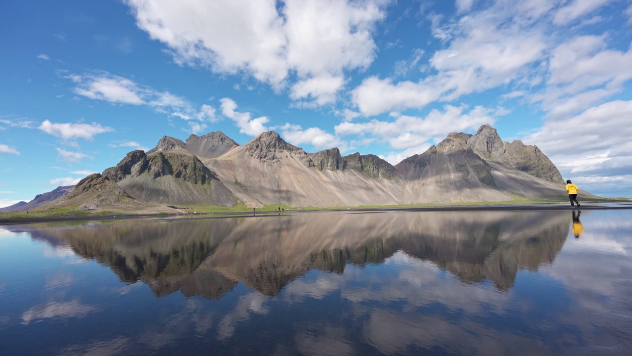 在冰岛Stokksnes半岛阳光明媚的黑色沙滩上，Vestrahorn山的景观与游客的旅行反射视频素材