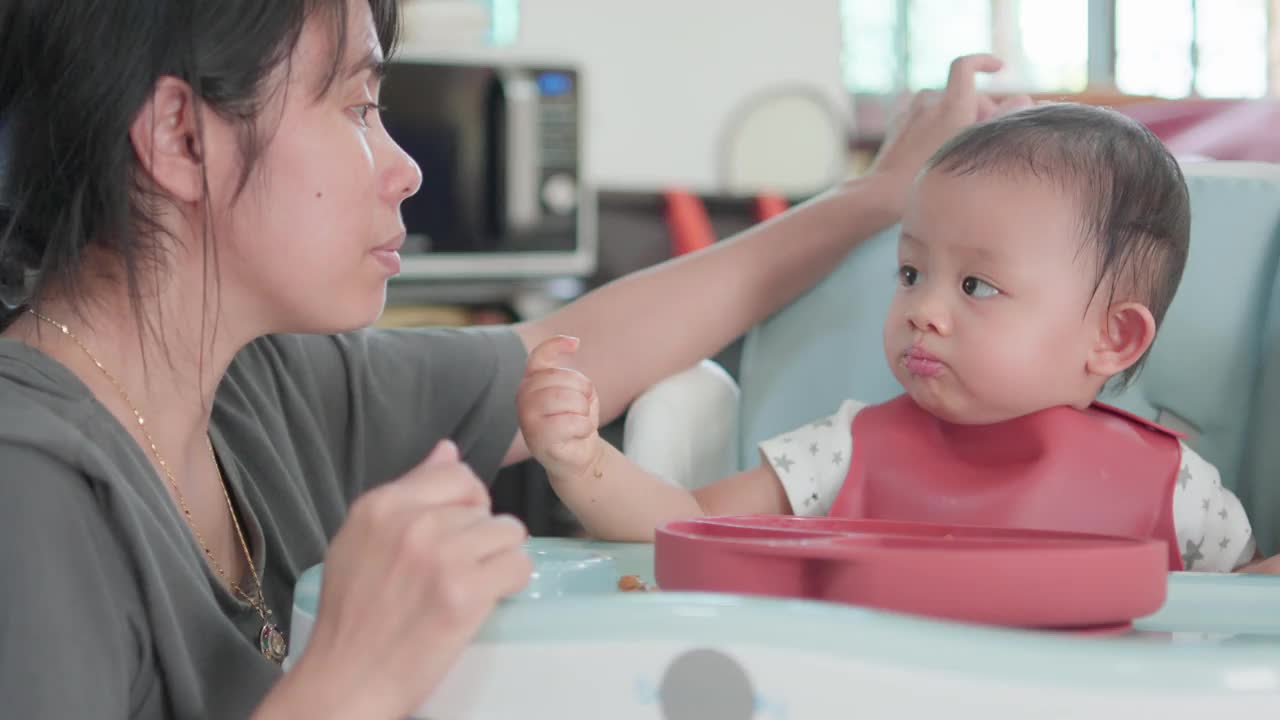 真实的照片可爱的亚洲新生儿和妈妈坐在高脚椅上吃饭视频素材