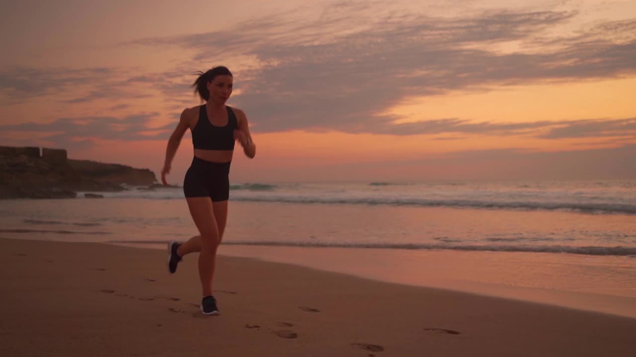 运动的女人慢跑在海洋海滩上日落的背景视频素材