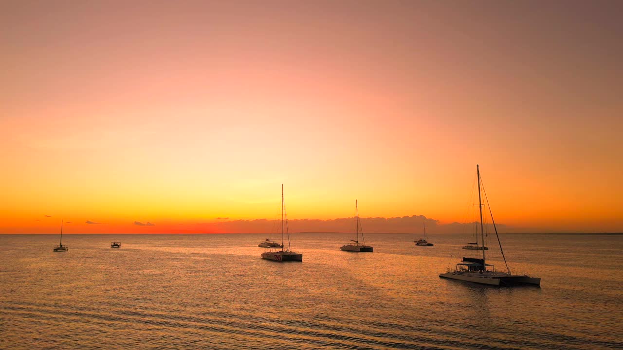 金色夕阳下停泊的旅游帆船与高桅杆双体船之间的空中飞行。平静的海面上，美丽的自然景观视频素材