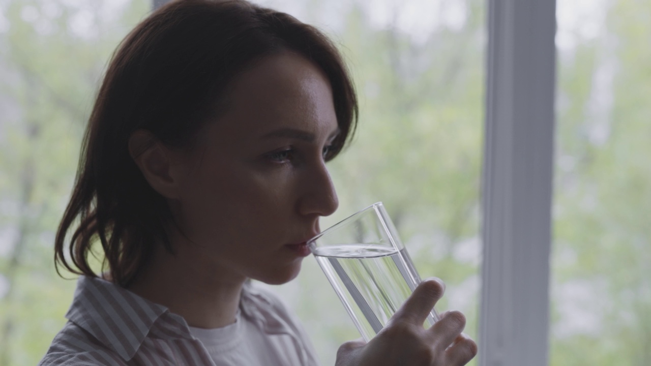 一个女人在喝一杯水。公寓里的房子。视频素材