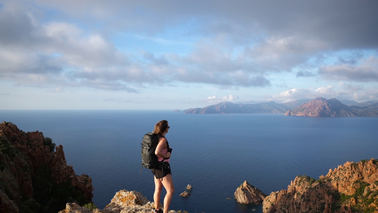 一位女性徒步旅行者站在视点上眺望夕阳下的海洋和悬崖海岸线视频素材