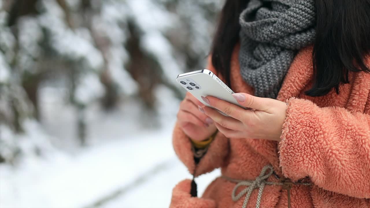 近女孩手与智能手机在冬季雪地公园在寒冷的天气滚动短信聊天用手机视频下载