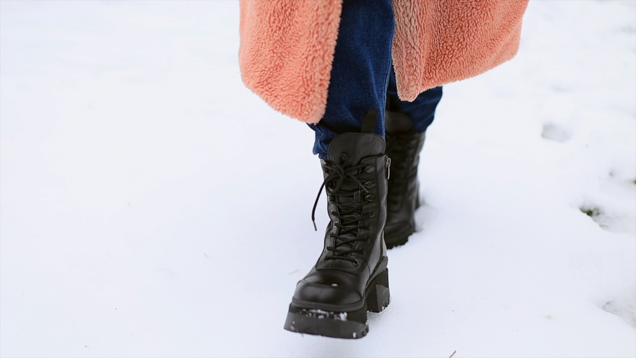 在雪地上穿着冬季鞋子和蓝色牛仔裤的女性腿部特写。视频素材