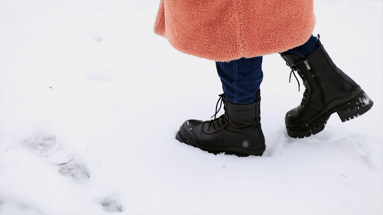 在雪地上穿着冬季鞋子和蓝色牛仔裤的女性腿部特写。视频素材