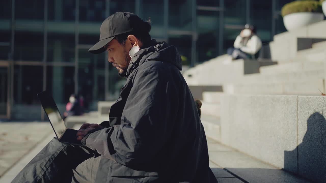 年轻的亚洲男人在城里用笔记本电脑。视频素材