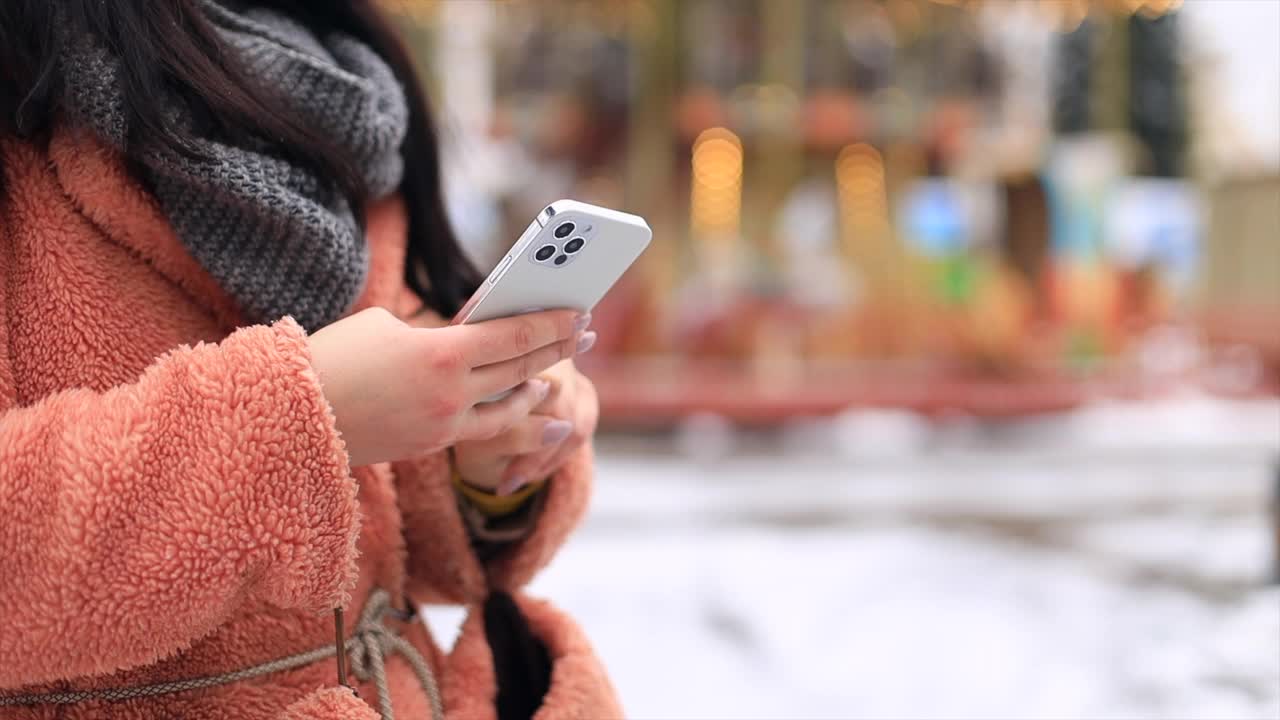 近女孩手与智能手机在冬季雪地公园在寒冷的天气滚动短信聊天用手机视频下载