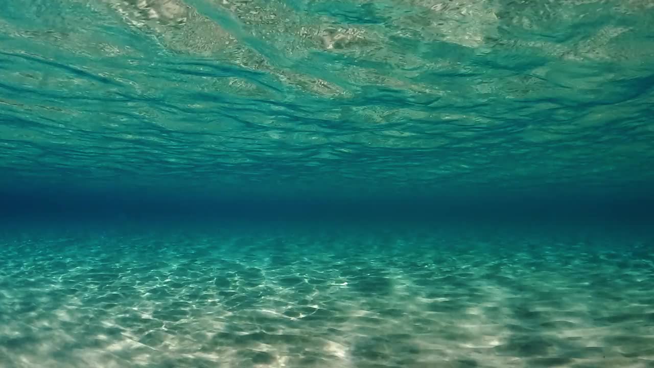 令人惊叹的水下水晶绿松石热带海水与涟漪表面和反射在海底与蓝色背景。慢动作视频素材