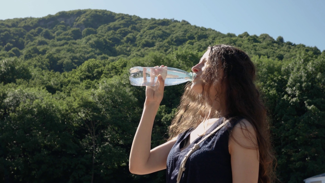 夏天，女人在山的背景下从瓶子里喝水视频下载