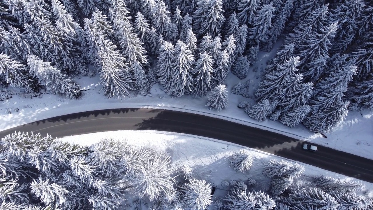 冬季山路上行驶的汽车。鸟瞰白雪皑皑的森林与道路。视频素材