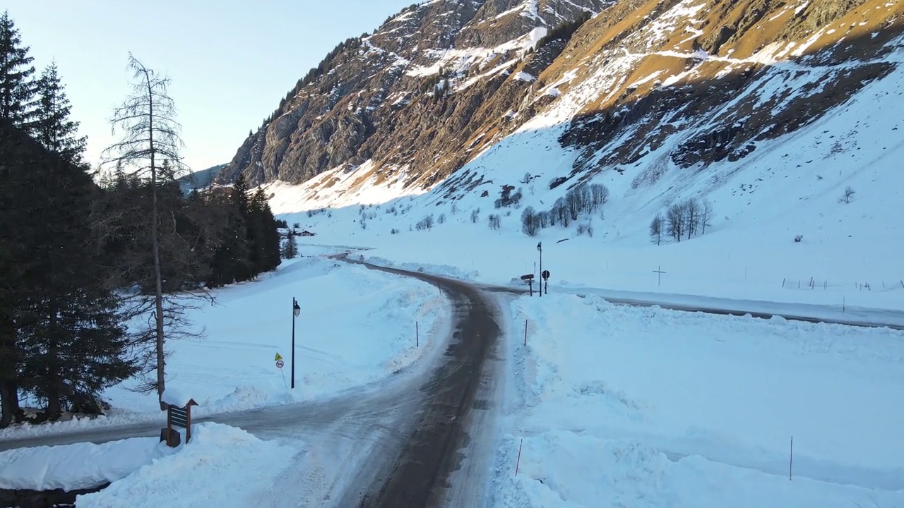 无人机俯瞰瑞士阿尔卑斯山脉中心的冰川狭窄道路，冬季被冰雪覆盖的狭窄道路分隔的小度假村，通往旅行目的地的山脉道路全景。壮丽的冬季瑞士阿尔卑斯山视频素材