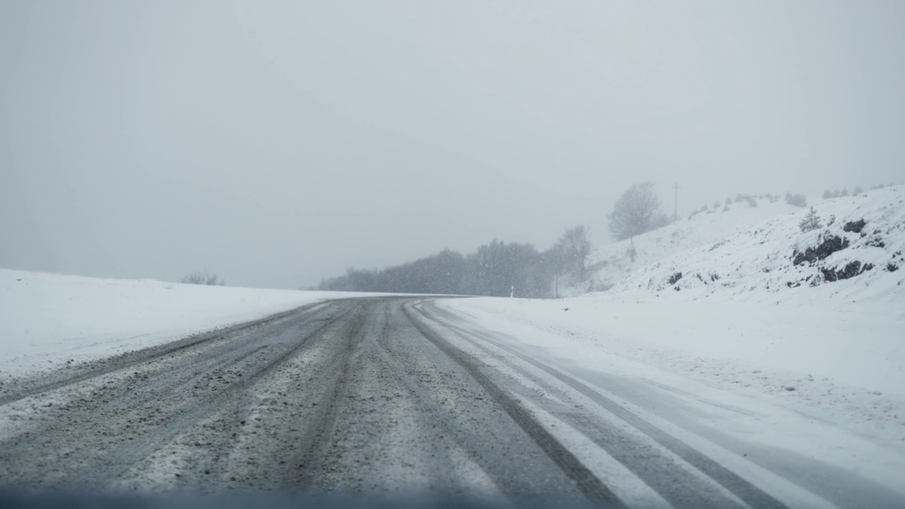 POV在大雪中沿着乡村道路行驶，周围有冬天的树木，慢动作视频素材