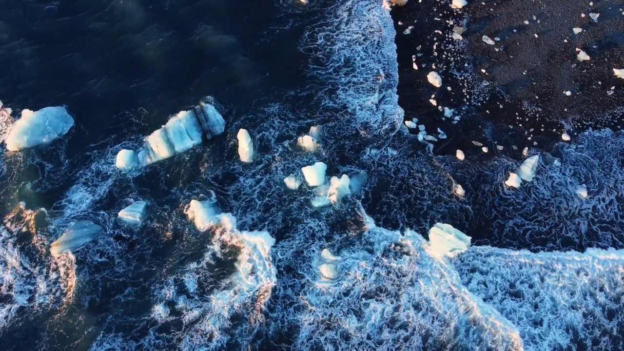 在冰岛的火山海滩，纯蓝色的海水海浪粉碎了日落时的冰川视频素材