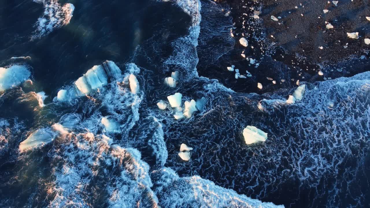 在冰岛的火山海滩，纯蓝色的海水海浪粉碎了日落时的冰川视频素材