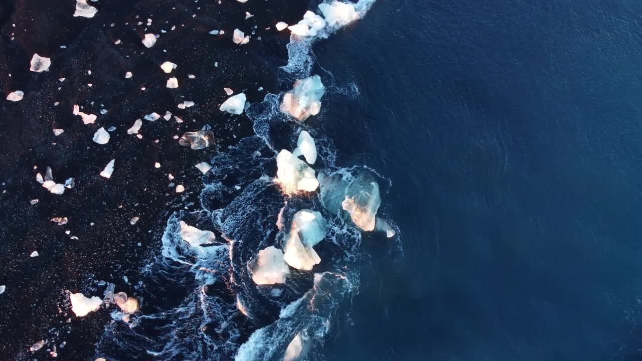 在冰岛的火山海滩上，纯蓝色的海浪带着光的反射粉碎了冰山视频素材