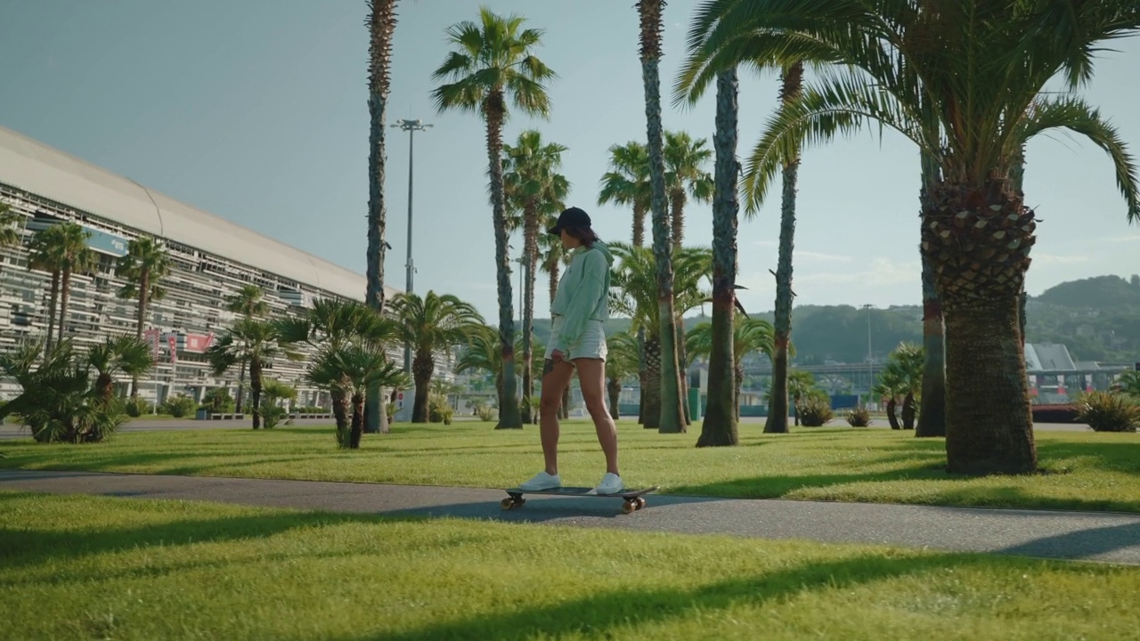 夏天在城市的街道上骑长板，年轻的运动女子在公园里骑滑板视频素材