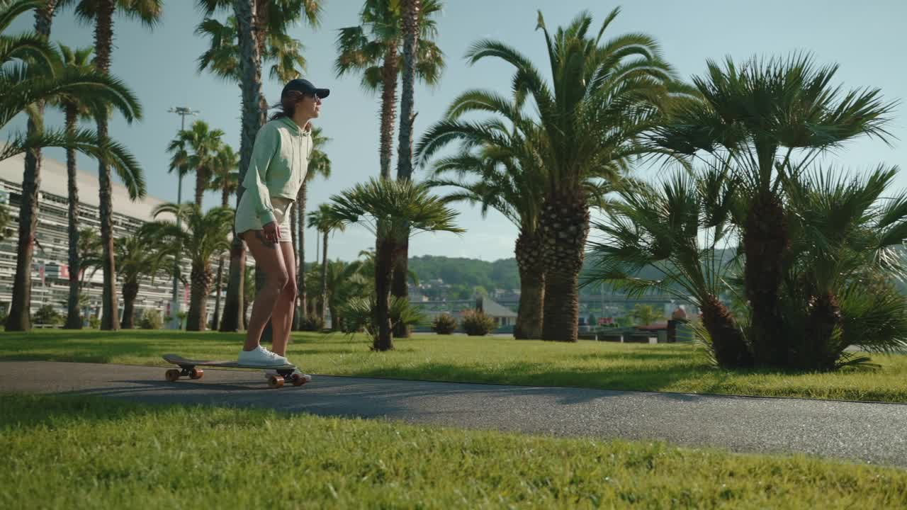 快乐的年轻女子在炎炎夏日的城市街道上骑滑板，慢镜头视频素材