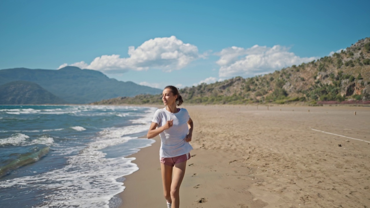 运动的女人跑海洋海滩。年轻的白人女性锻炼户外跑步海滨。健康跑步和户外运动的概念。积极运动的运动员慢跑。夏季活跃。视频素材