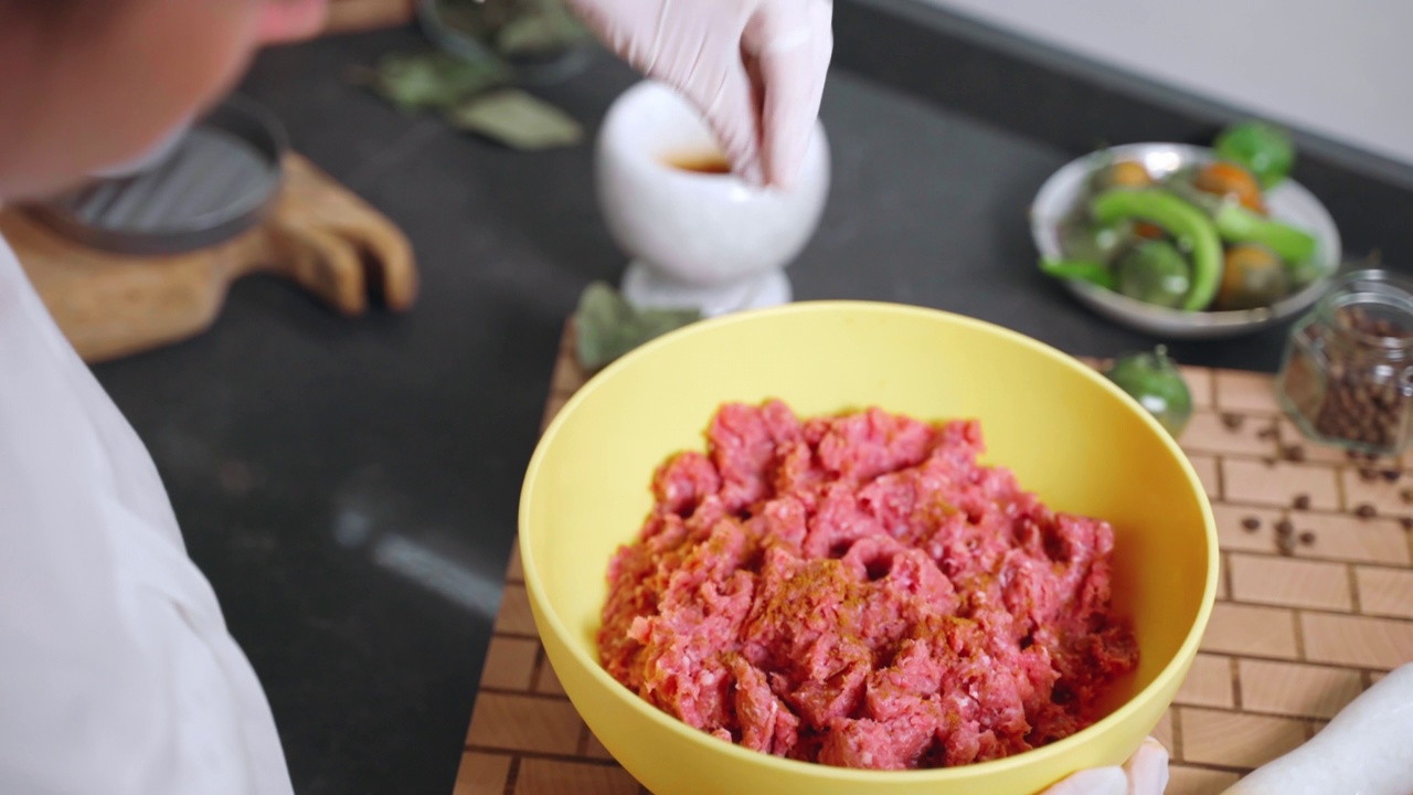 戴手套的女子在黄色的碗里调味生拌肉末和香料粉。在做汉堡、肉排或肉丸之前加入盐、胡椒粉和辣椒粉。肉类配方中的芳香原料，烹饪中的香料和香草视频素材