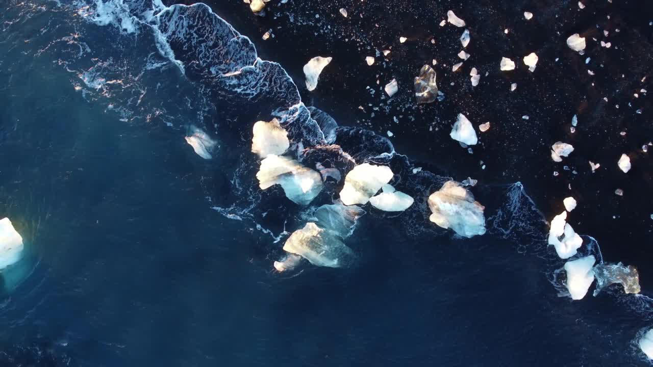 在冰岛的火山海滩上，纯蓝色的海浪带着光的反射粉碎了冰山视频素材