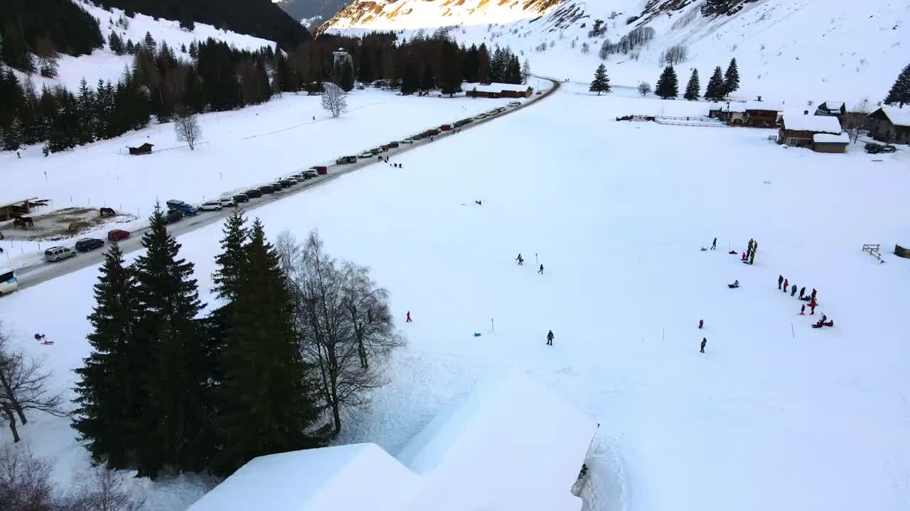 瑞士冬季度假胜地在令人惊叹的阿尔卑斯山脉，鸟瞰岩石山脉脚下的瑞士小村庄，人们滑雪，孩子们在白雪覆盖的操场上雪橇，家庭度假时间在冰冻的阿尔卑斯山脉，瑞士在赢视频素材